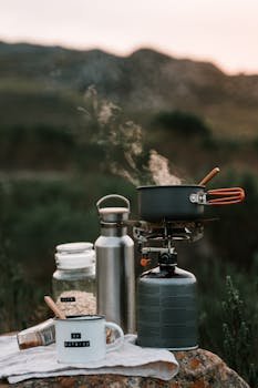 A picturesque outdoor camping scene with cooking gear and steam rising from a pot at sunrise.
