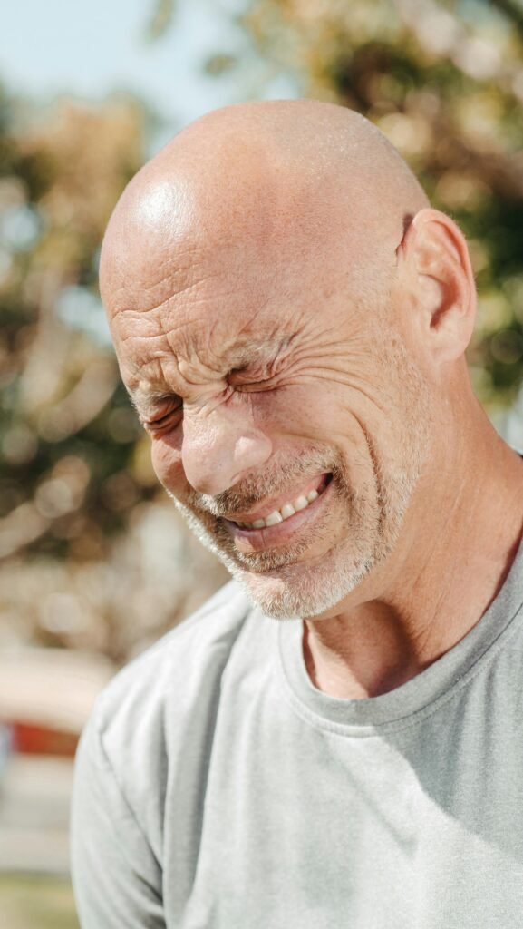 An elderly man with a pained expression captured in natural sunlight outdoors.